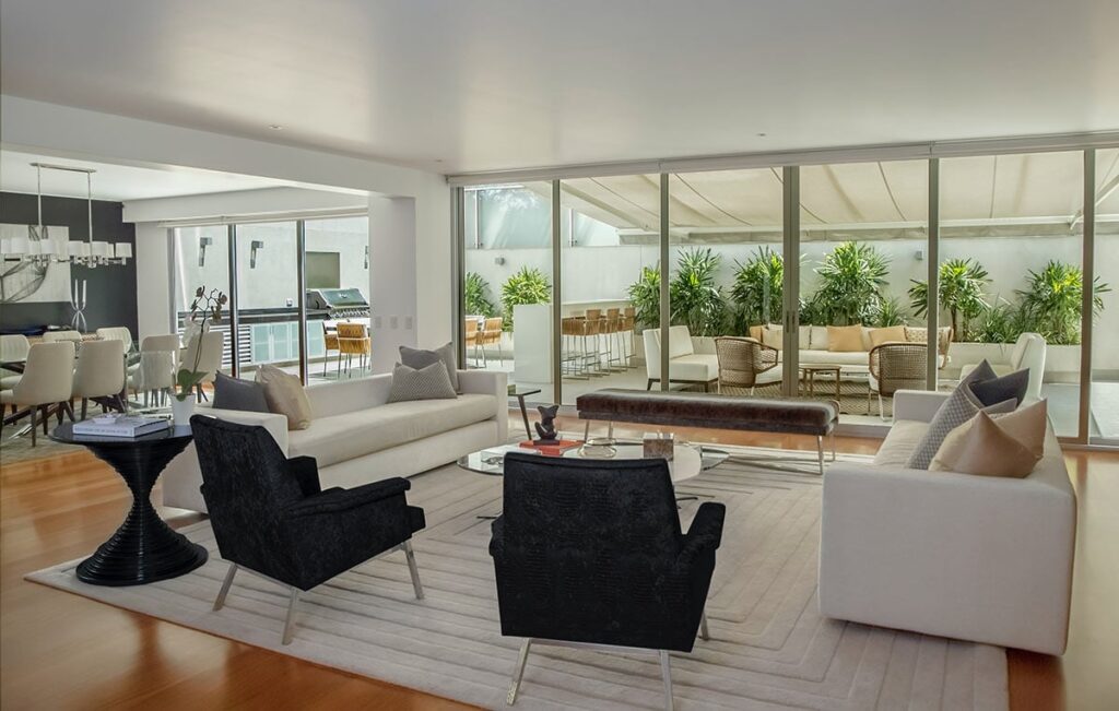 Modern living room with neutral furniture and view of outdoor patio surrounded by greenery