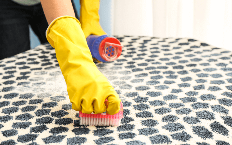An image of cornstarch sprinkled over a greasy stain on a fabric sofa, with a vacuum nearby.