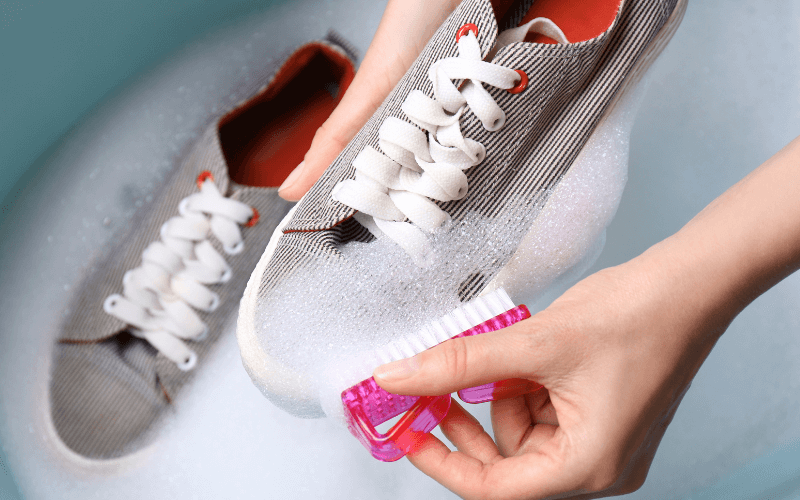 Image of hands cleaning a dirty shoe using a brush. The shoe is covered in foamed-up soapsolution, with a towel underneath.