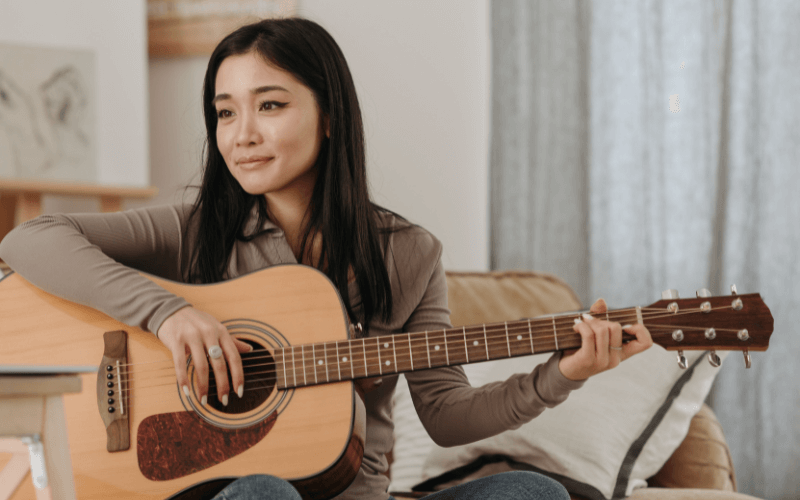 Image of a person playing a guitar inside their living room.