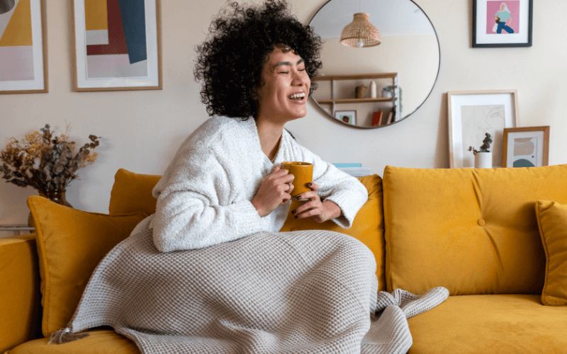 Image of a person sitting down on their couch, holding a cup of coffee, and with their eyes closed.