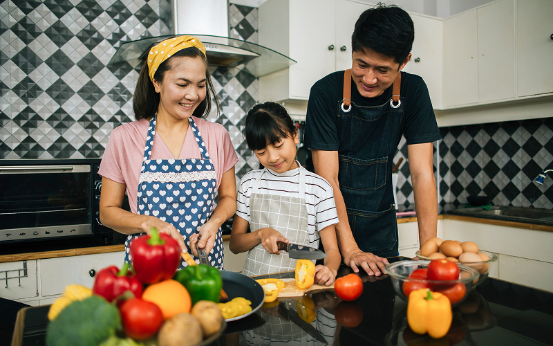 A family in a kitchen while parents are cooking and kids are around.