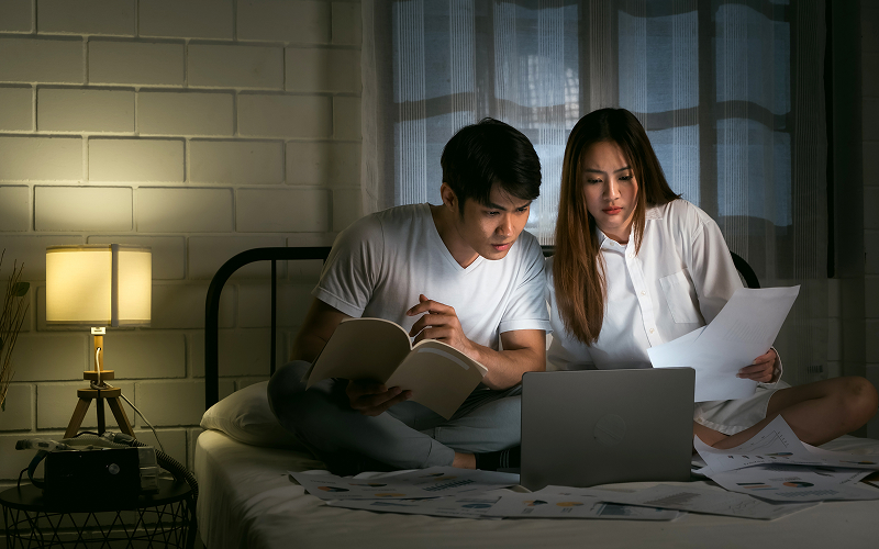 A young couple reading or relaxing in a warm industrial-styled HDB bedroom.