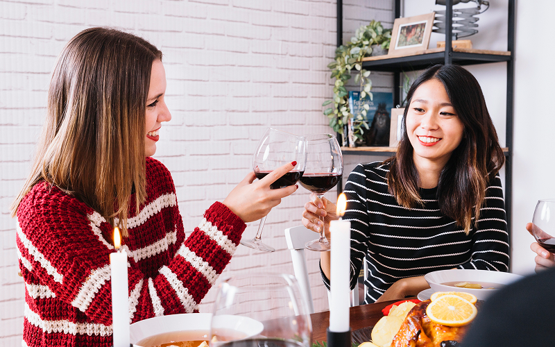Two people clinking two wine glasses in a kitchen.