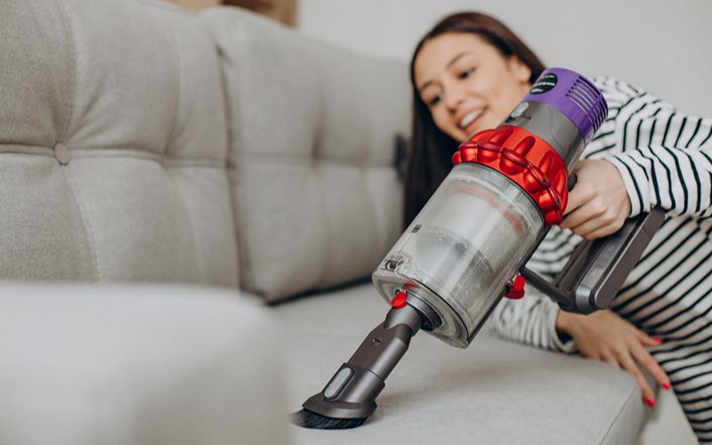 A person using a cordless vacuum cleaner on a sofa